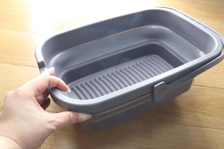 女性の手が折り畳まれたたらいを広げている途中の様子。