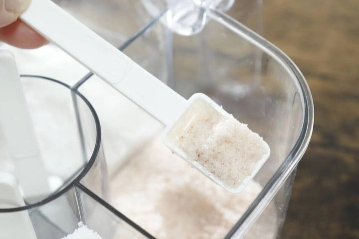 調味料ポットに入った塩を白い計量スプーンで山盛りすくっている手元。