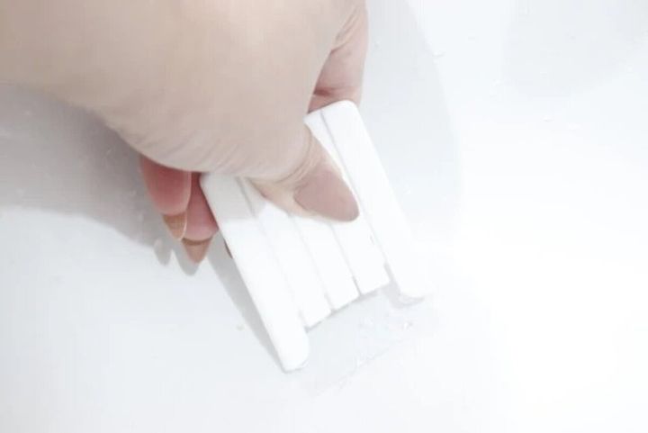 白いスクレーパーを湾曲させて白い面に付いた汚れをこそぎ落とす手元