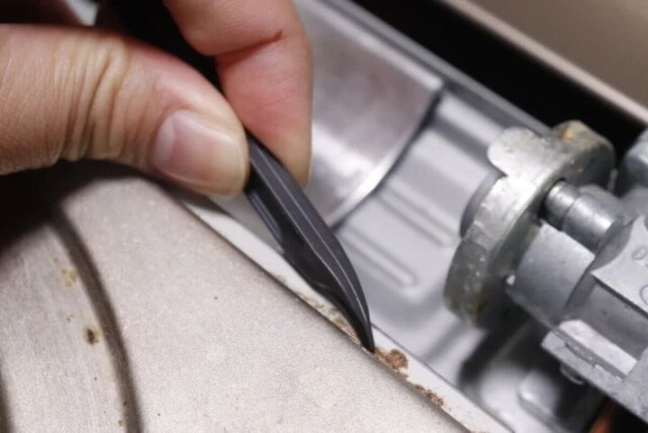 ガスコンロのバーナー周りの隙間をカーブした使い捨てヘラで掃除する手元
