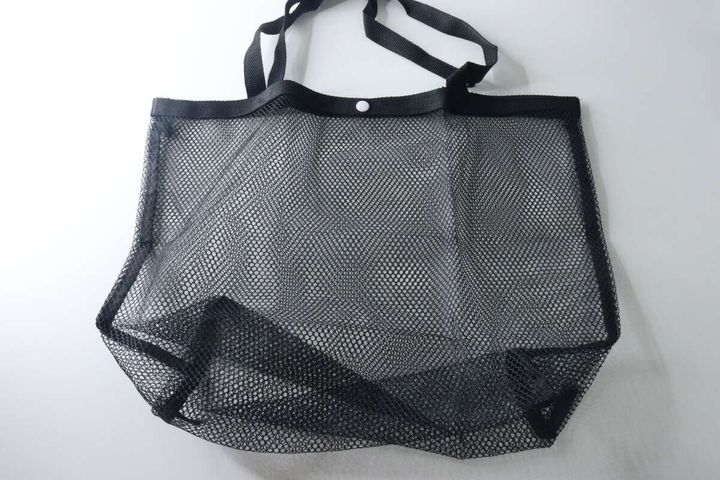 広げられた黒いメッシュバッグ。上部に白いスナップボタンが見える