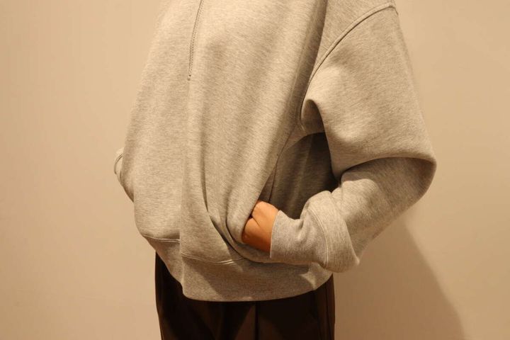 グレーのハーフジップスウェットのポケットに手を入れる女性