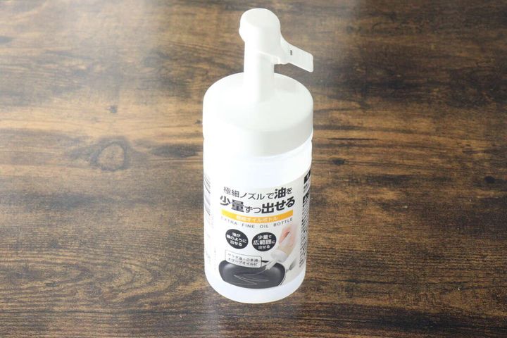 白い極細オイルボトルが木目のテーブルに置かれ、商品の説明シールが貼られている