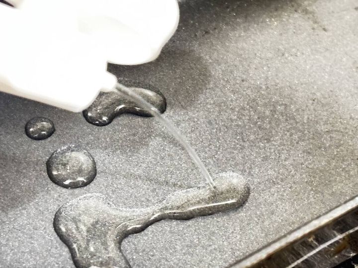 白い極細オイルボトルからフライパンに細く油が注がれ、数カ所に油滴が落ちている