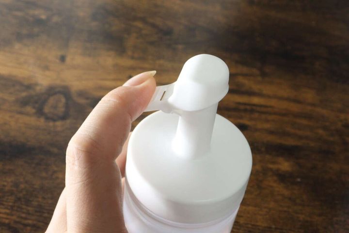 女性の指が白いオイルボトルのキャップを閉じ、注ぎ口を収納している