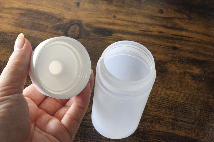 女性の手が白い極細オイルボトルの蓋を開け、本体と蓋が分離している