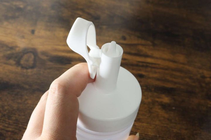 女性の指が白いオイルボトルのキャップの突起を押し、注ぎ口を出している