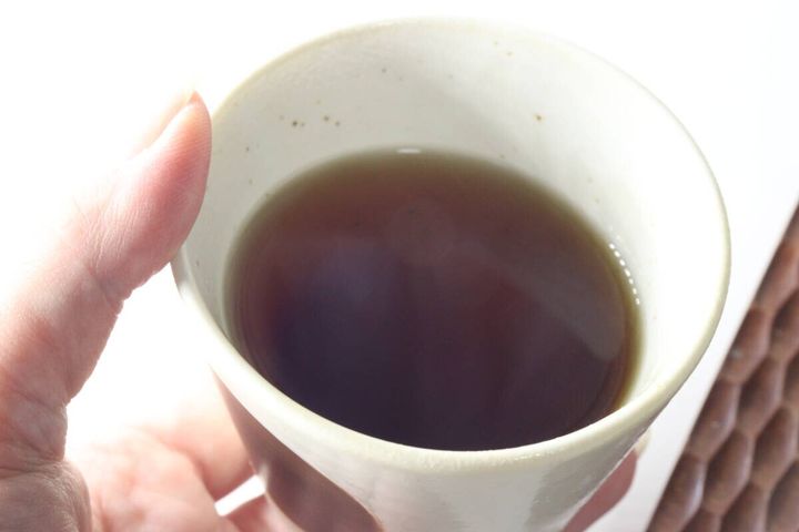 女性がやきいも茶の入った湯呑み茶碗を持ち上から覗き込んでいる