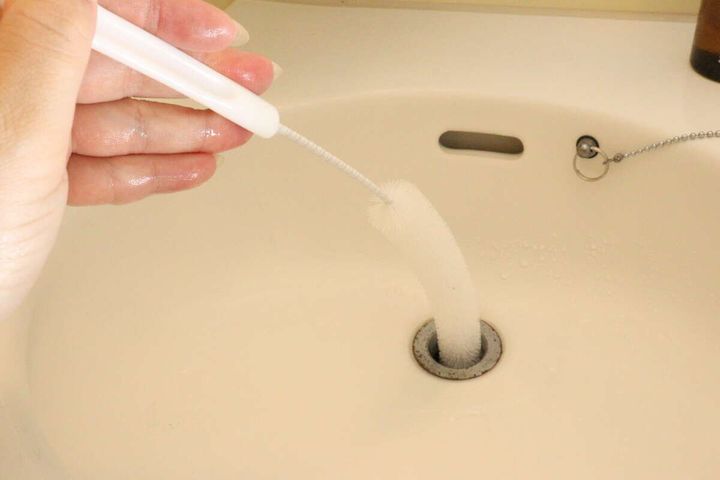 女性が洗面台の排水口にパイプクリーナーを差し込んでいる