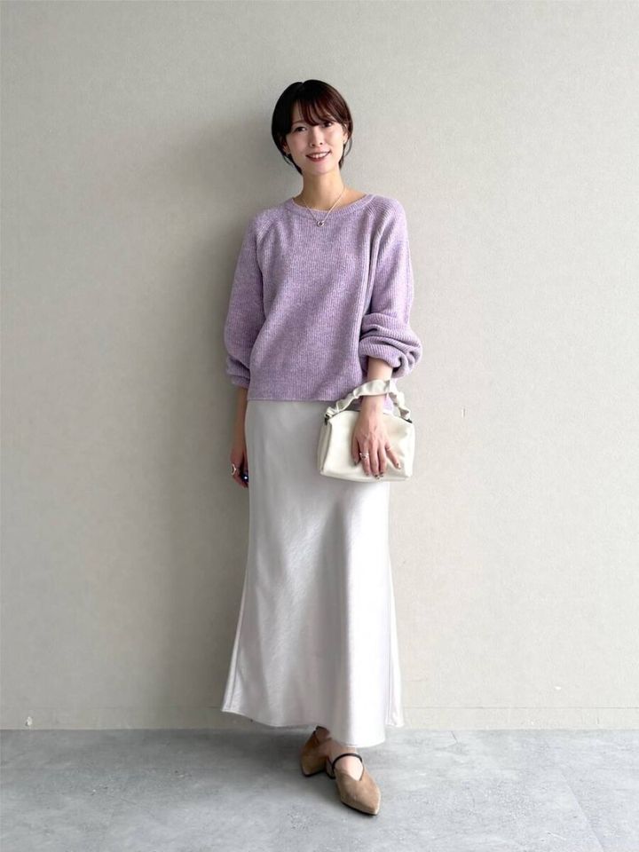淡いパープルニットと白サテンスカートを着用した女性