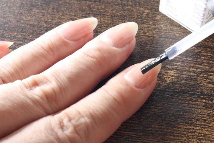 人差し指の爪にネイル速乾剤のハケで透明な液を塗っている手元
