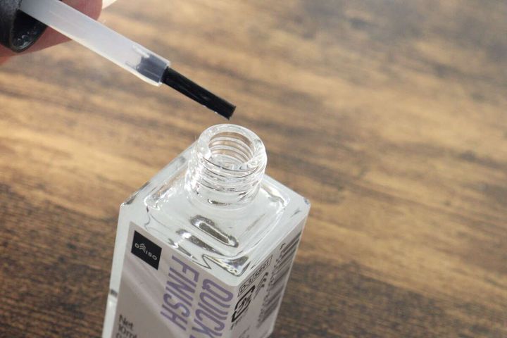 ネイル速乾剤のボトルから透明な液がついたハケを取り出している手元