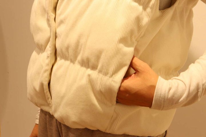 オフホワイトのコーデュロイベストのポケットに手を入れている