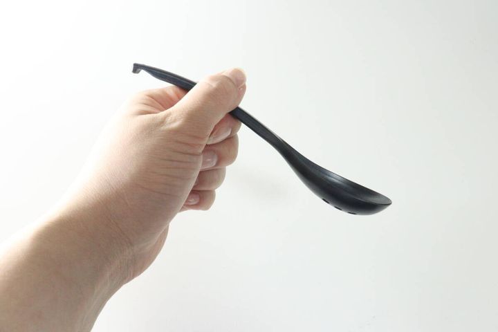 女性の手が黒い穴あきレンゲを握って持っている