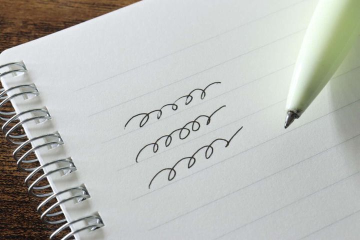 ノートの罫線に黒いボールペンで試し書きをしている様子