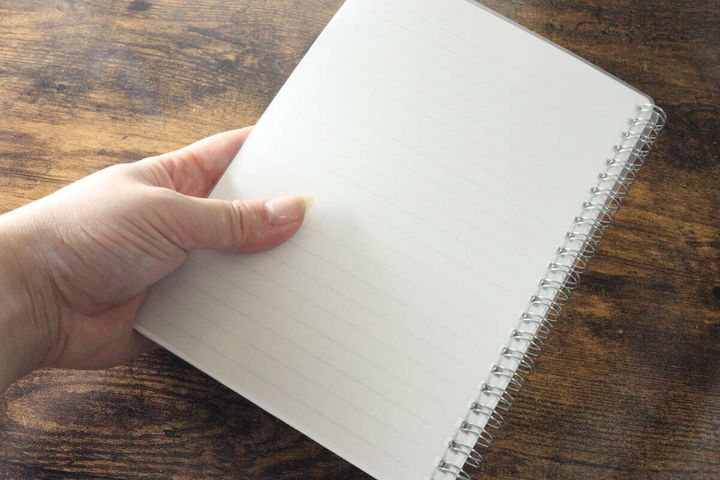 女性の手が罫線が引かれたリングノートのページを持っている