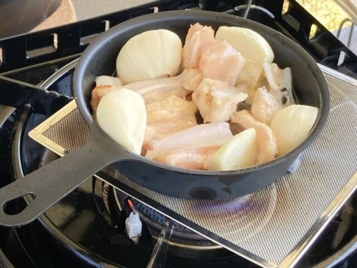 バーナーパッドを敷いたバーナーで鶏肉と玉ねぎを調理する鍋