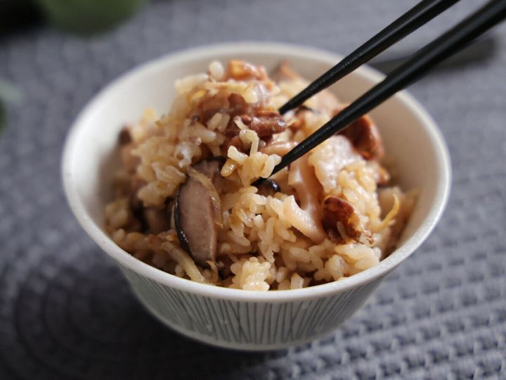 茶碗に盛られた炊き込みごはんを黒い箸でつまみ上げているクローズアップ。