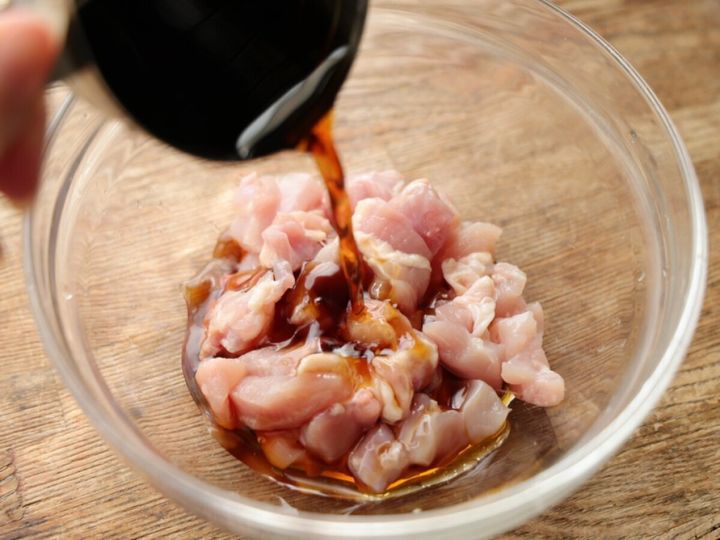 透明なボウルに入った角切り鶏もも肉にめんつゆを注ぎ入れている様子。