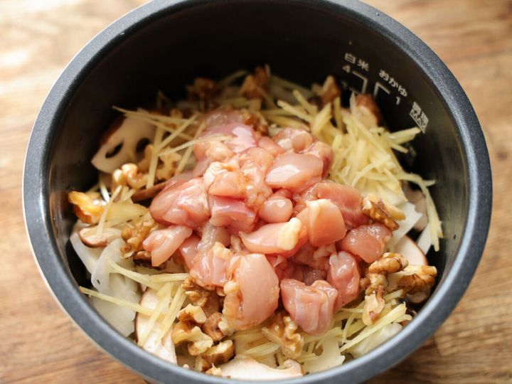炊飯器の内釜に研いだ米を入れ、その上に鶏肉、蓮根、しいたけ、生姜、くるみを乗せている。