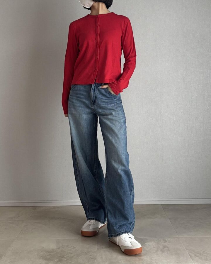 赤のポインテールカーディガンと薄色デニムワイドパンツ、白スニーカーの女性