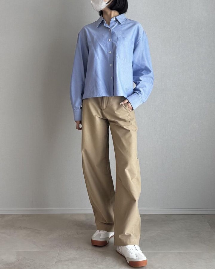 水色のオックスフォードシャツとベージュワイドパンツ、白スニーカーを履いた女性