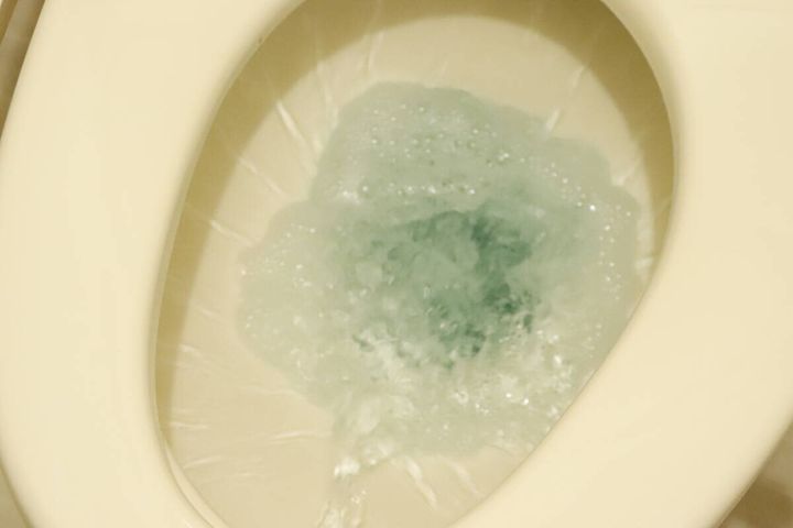 トイレの便器に薄い青色の水が勢いよく流れている様子