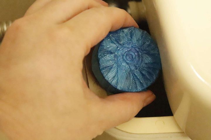 トイレタンクの給水口を避けて青い固形洗剤を入れている手