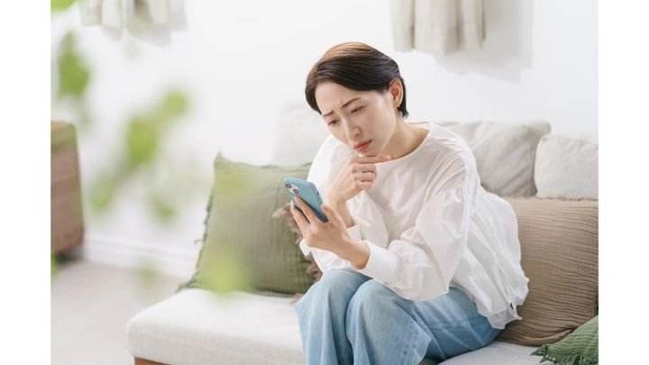 ソファに座り、悩ましい表情でスマホを見る女性