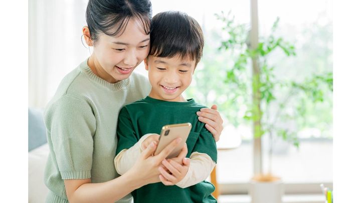 親子で寄り添いながらスマートフォン画面を見る母親と男の子