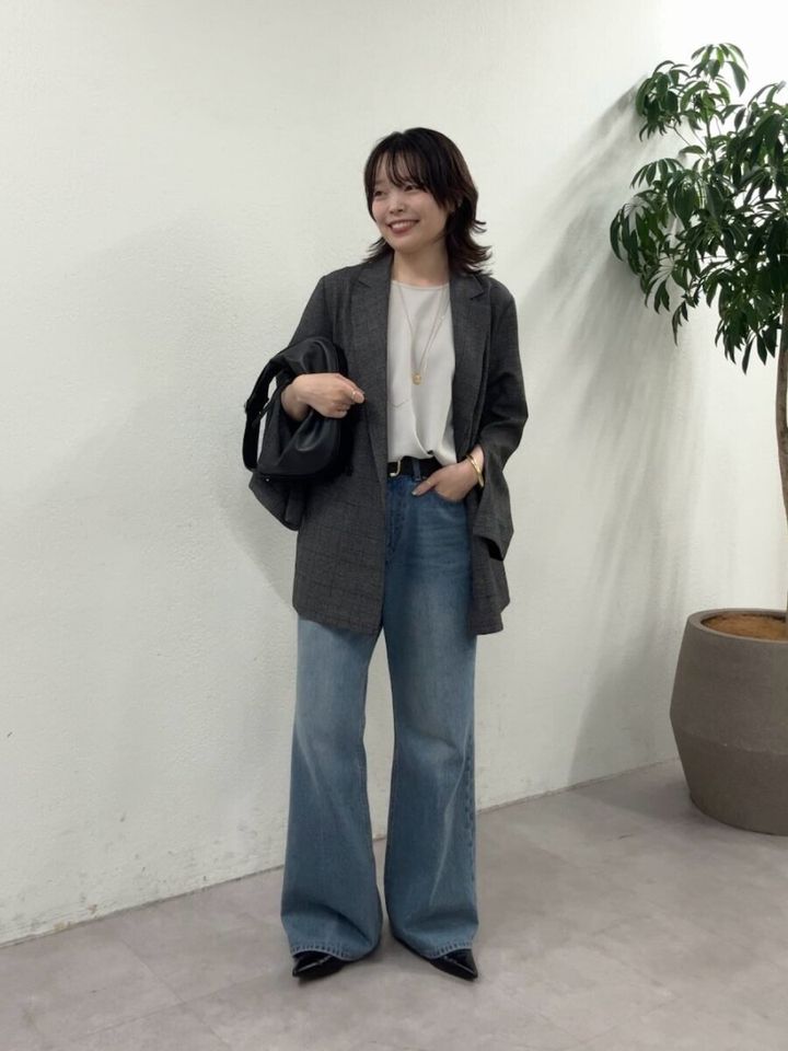 グレーのジャケットと白トップス、デニムを着用し笑顔で立つ女性
