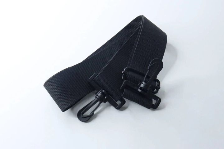 黒い幅広のショルダーバッグストラップが白い背景に置かれている