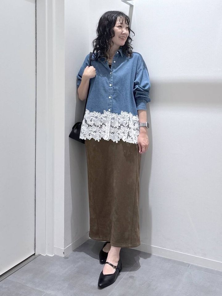 切り替えレースデニムシャツを着た女性が茶色スカートと黒いバッグを合わせている