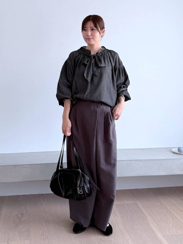 濃いグレーのボウタイブラウスを着た女性が同系色ワイドパンツと黒いバッグを持つ