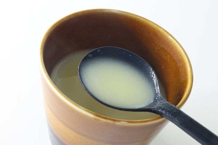 茶色のカップに入ったコーンポタージュを黒いスプーンですくっている