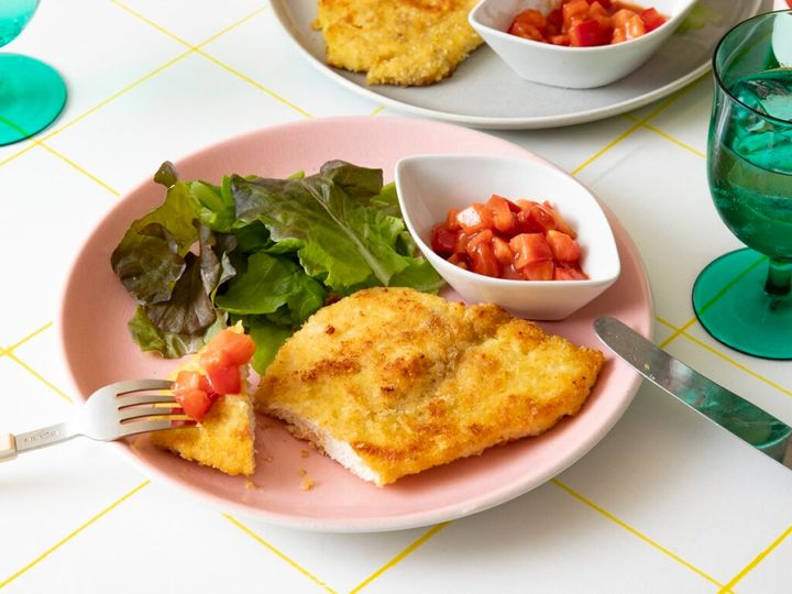 お皿に鶏むね肉のシュニッツェル、リーフサラダ、トマトソース。傍らにワイングラス
