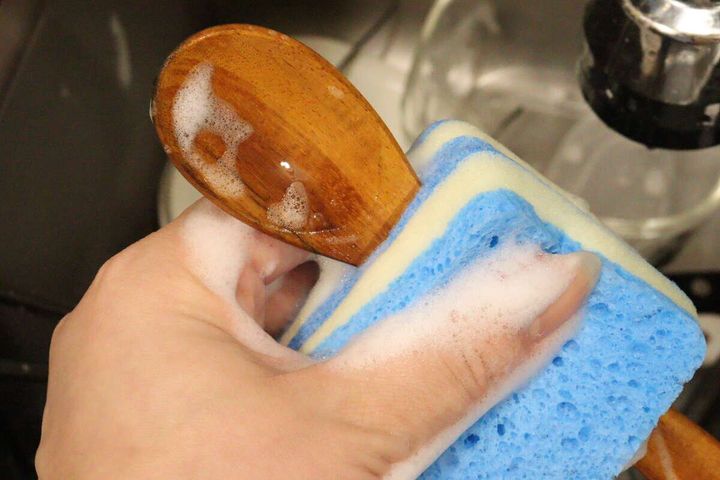 泡立ったスポンジで木製スプーンを挟んで洗っている様子