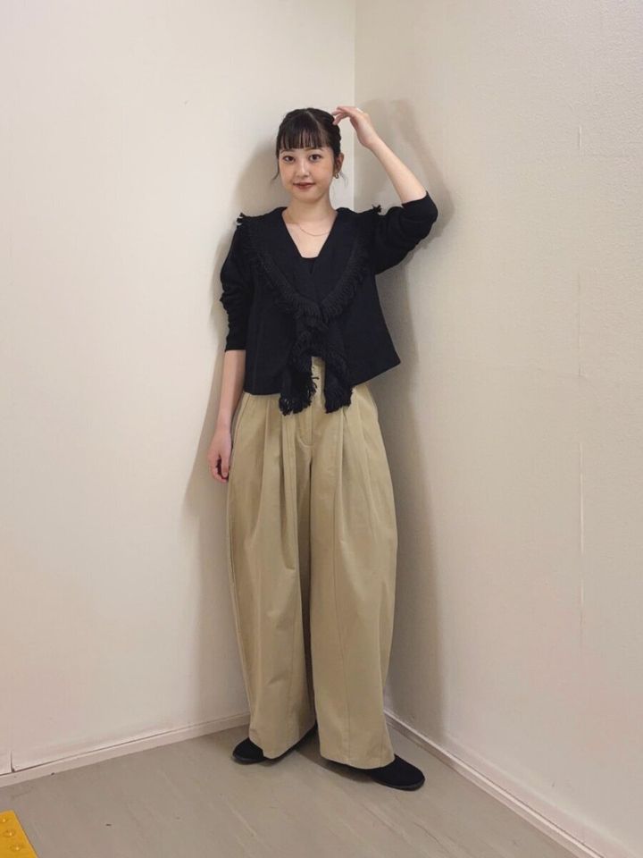 Vネック黒ブラウスとベージュワイドパンツの女性、壁際で立つ