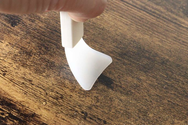 手が三角形の白いミニスパチュラを持ち先端を木目調のテーブルに当てている