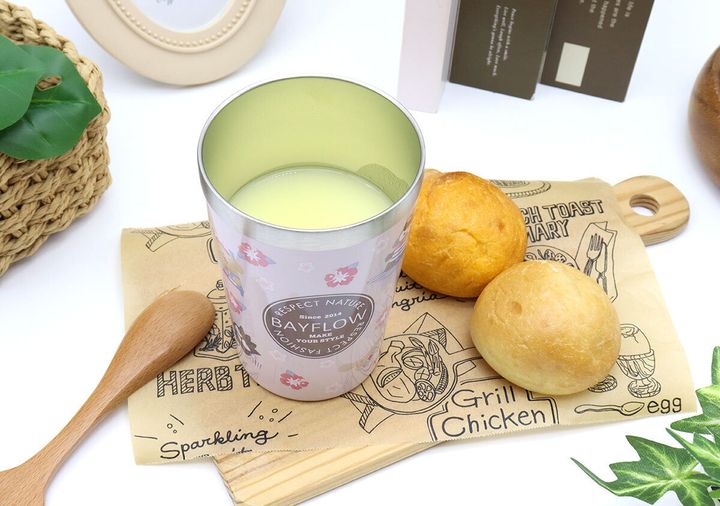 ピンクタンブラーに飲み物、パン、木製スプーンが置かれたテーブル