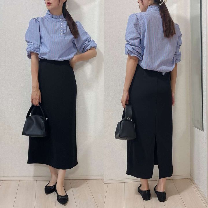 青いブラウスと黒タイトスカートを着た女性が黒いバッグを持つ