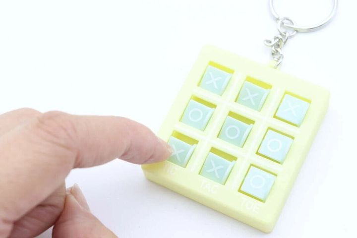 黄色いマルバツゲームキーホルダーの盤面を指で操作している手元