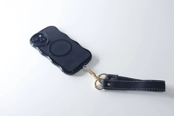 白い背景で黒いスマホに装着された黒い合皮のワイドストラップ