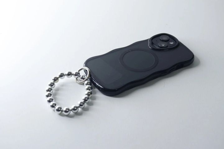 白い背景で黒いスマホに装着されたシルバーのブレスレット風ストラップ