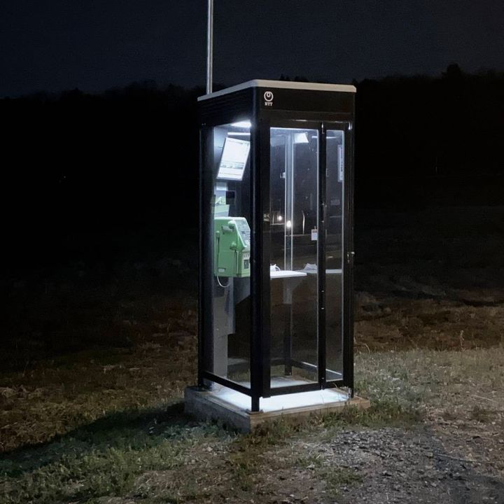暗い夜道にぽつんと立つ、明かりのついた公衆電話ボックス。