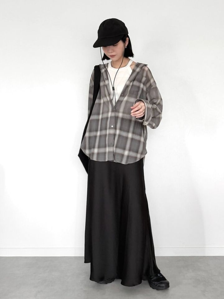 透け感グレーチェックシャツと黒ロングスカートの女性