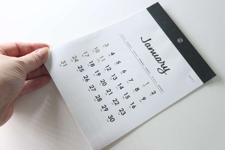 女性が壁掛けカレンダーのページをめくる手元