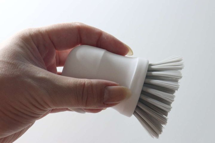 女性の手で白いハンドキッチンブラシを上から握っている様子