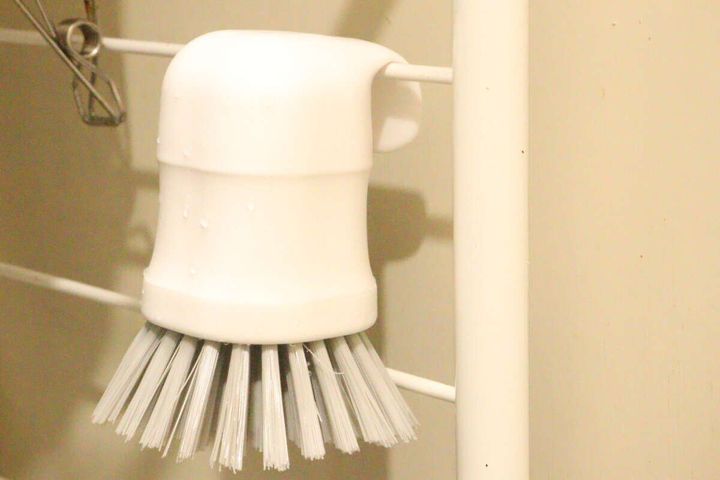水滴がついた白いハンドキッチンブラシが、フックでバーに吊るされている様子