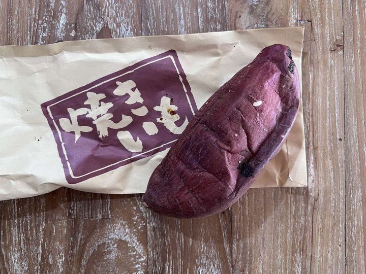 茶色い紙袋に入った焼き芋が木目のテーブルに置かれている